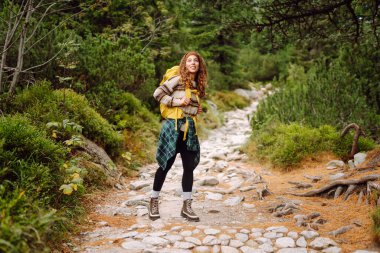 Dağ manzaralı kayalık patikada sarı sırt çantalı genç bayan yürüyüşçü. Mutlu kadın hava ve açık hava macerasını seviyor. Seyahat kavramı.
