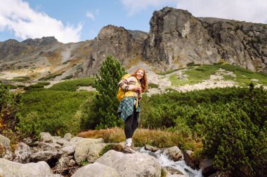 Dağ manzaralı kayalık patikada sarı sırt çantalı genç bayan yürüyüşçü. Mutlu kadın hava ve açık hava macerasını seviyor. Seyahat kavramı.