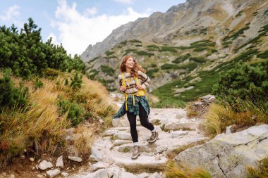 Dağ manzaralı kayalık patikada sarı sırt çantalı genç bayan yürüyüşçü. Mutlu kadın hava ve açık hava macerasını seviyor. Seyahat kavramı.