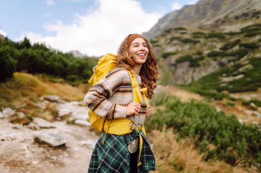 Dağ manzaralı kayalık patikada sarı sırt çantalı genç bayan yürüyüşçü. Mutlu kadın hava ve açık hava macerasını seviyor. Seyahat kavramı.
