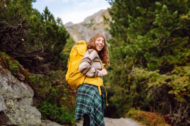 Dağ manzaralı kayalık patikada sarı sırt çantalı genç bayan yürüyüşçü. Mutlu kadın hava ve açık hava macerasını seviyor. Seyahat kavramı.