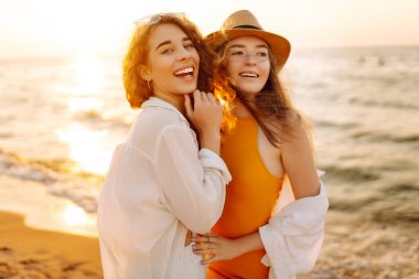 Neşeli iki bayan arkadaş deniz kıyısında gün batımının tadını çıkarıyorlar. Özgürlüğü hisseden, dışarıda yürüyen güzel kadınlar. Arkadaşlık kavramı, eğlence..