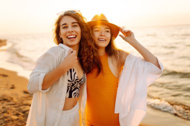 Neşeli iki bayan arkadaş deniz kıyısında gün batımının tadını çıkarıyorlar. Özgürlüğü hisseden, dışarıda yürüyen güzel kadınlar. Arkadaşlık kavramı, eğlence..