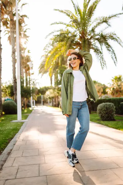 Güneşli şehir caddesinde gün batımında yürüyen güzel bir kadın. Sırt çantalı ve güneş gözlüklü mutlu turist dışarıda havanın tadını çıkarıyor. Hafta sonu ve eğlence konsepti.