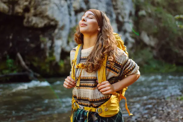 Sırt çantalı genç bir kadın dağ nehri yakınlarındaki dağ manzarasının tadını çıkarıyor. Mutlu kadın gezgin özgürlüğü hisseder, dağlarda yol boyunca yürür. Yürüyüş ve doğa konsepti.