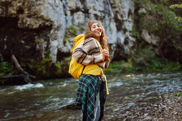 Sırt çantalı genç bir kadın dağ nehri yakınlarındaki dağ manzarasının tadını çıkarıyor. Mutlu kadın gezgin özgürlüğü hisseder, dağlarda yol boyunca yürür. Yürüyüş ve doğa konsepti.