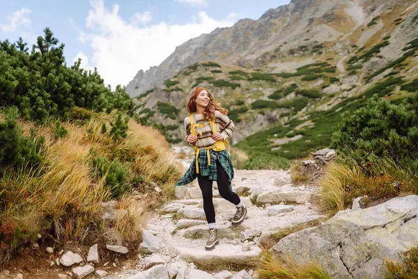 Dağ manzaralı kayalık patikada sarı sırt çantalı genç bayan yürüyüşçü. Mutlu kadın hava ve açık hava macerasını seviyor. Seyahat kavramı.