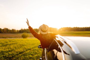 Seyahat tutkusu. Pencereden sarkan şapkalı mutlu bir gezgin. Gün batımında özgürlük hisseden genç bir kadın. Macera konsepti.