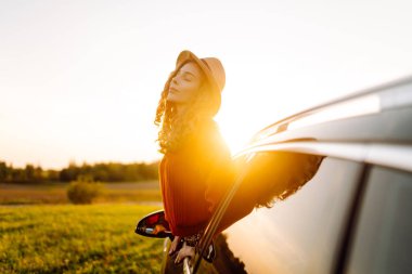 Seyahat tutkusu. Pencereden sarkan şapkalı mutlu bir gezgin. Gün batımında özgürlük hisseden genç bir kadın. Macera konsepti.