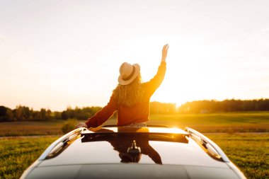 Seyahat tutkusu. Pencereden sarkan şapkalı mutlu bir gezgin. Gün batımında özgürlük hisseden genç bir kadın. Macera konsepti.