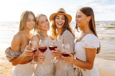 Dört bayan arkadaş sahilde birlikte eğleniyor, şarap içiyor ve bir paspasın üzerinde dinleniyorlar. Güzel kadınlar sahilde günbatımının tadını çıkarıyorlar. Arkadaşlık ve rahatlama kavramı.