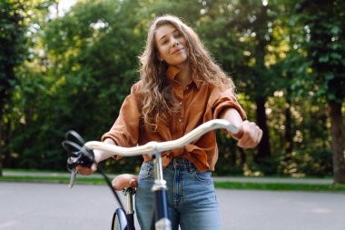 Yeşil bir parkta bisiklet süren genç bir kadın. Neşeli kadın hafta sonunun tadını çıkarıyor, gün batımında bisiklet sürüyor. Aktif yaşam tarzı. Joy, hafta sonu konsepti.
