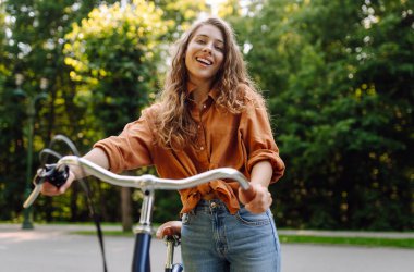 Yeşil bir parkta bisiklet süren genç bir kadın. Neşeli kadın hafta sonunun tadını çıkarıyor, gün batımında bisiklet sürüyor. Aktif yaşam tarzı. Joy, hafta sonu konsepti.