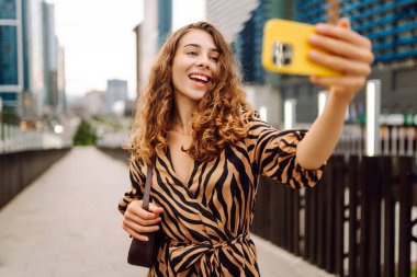 Selfie zamanı! Elinde telefon olan güzel bir kadın arka planda şehirle birlikte gezinti güvertesinde yürüyor. Genç turist blogları ve açık havada selfie çekiyor. Turizm ve blog kavramı.
