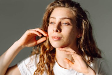 Kıvırcık saçlı genç bir kadın yüzüne hafifçe dokunuyor. Güzel bir kadın sıcak bir odada güneş ışınlarından hoşlanır. Doğallık, güzellik ve rahatlama kavramı..