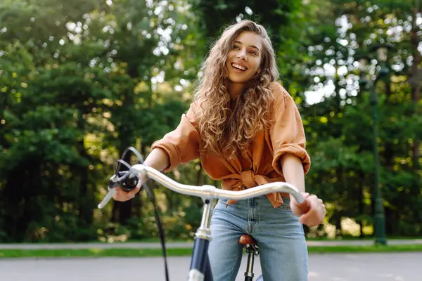 Yeşil bir parkta bisiklet süren genç bir kadın. Neşeli kadın hafta sonunun tadını çıkarıyor, gün batımında bisiklet sürüyor. Aktif yaşam tarzı. Joy, hafta sonu konsepti.