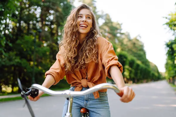 Yeşil bir parkta bisiklet süren genç bir kadın. Neşeli kadın hafta sonunun tadını çıkarıyor, gün batımında bisiklet sürüyor. Aktif yaşam tarzı. Joy, hafta sonu konsepti.