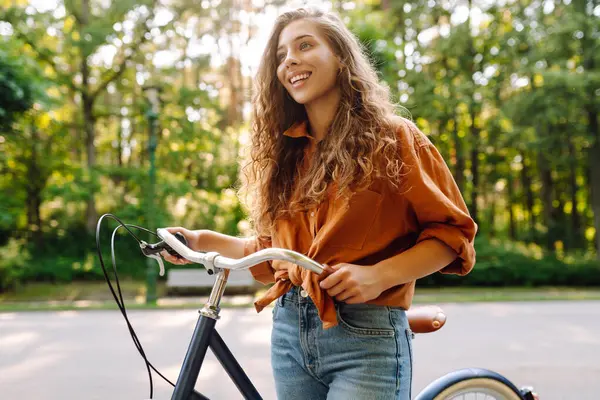 Yeşil bir parkta bisiklet süren genç bir kadın. Neşeli kadın hafta sonunun tadını çıkarıyor, gün batımında bisiklet sürüyor. Aktif yaşam tarzı. Joy, hafta sonu konsepti.