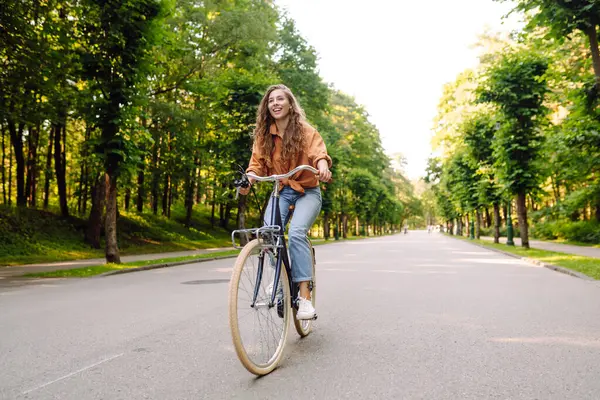 Yeşil bir parkta bisiklet süren genç bir kadın. Neşeli kadın hafta sonunun tadını çıkarıyor, gün batımında bisiklet sürüyor. Aktif yaşam tarzı. Joy, hafta sonu konsepti.