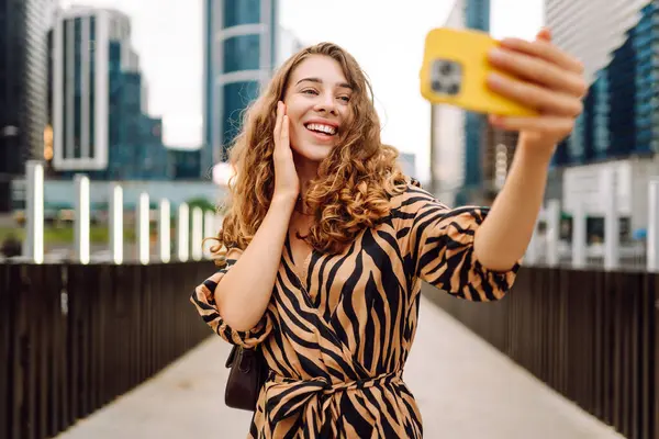 Selfie zamanı! Elinde telefon olan güzel bir kadın arka planda şehirle birlikte gezinti güvertesinde yürüyor. Genç turist blogları ve açık havada selfie çekiyor. Turizm ve blog kavramı.