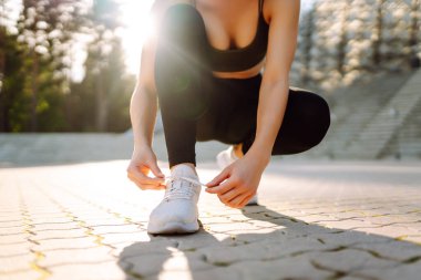 Eğitimden önce ayakkabı bağcıklarını bağlayan atletik kadının yakın çekimi. Spor giyimli genç bir kadın gün batımında egzersiz yapmadan önce hazırlanıyor. Spor konsepti. Etkin yaşam biçimi.