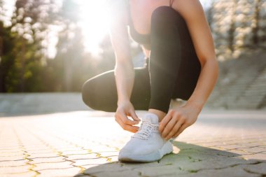 Eğitimden önce ayakkabı bağcıklarını bağlayan atletik kadının yakın çekimi. Spor giyimli genç bir kadın gün batımında egzersiz yapmadan önce hazırlanıyor. Spor konsepti. Etkin yaşam biçimi.