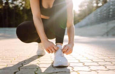 Eğitimden önce ayakkabı bağcıklarını bağlayan atletik kadının yakın çekimi. Spor giyimli genç bir kadın gün batımında egzersiz yapmadan önce hazırlanıyor. Spor konsepti. Etkin yaşam biçimi.