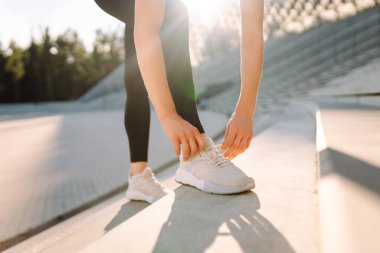 Eğitimden önce ayakkabı bağcıklarını bağlayan atletik kadının yakın çekimi. Spor giyimli genç bir kadın gün batımında egzersiz yapmadan önce hazırlanıyor. Spor konsepti. Etkin yaşam biçimi.