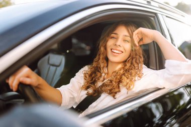 Beyaz bir kaşkorse içinde araba süren güzel kadın pencereden dışarı bakıyor. Genç bir kadın araba kullanıyor ve güneşli havanın tadını çıkarıyor. Ulaşım, seyahat, taksi kavramı.