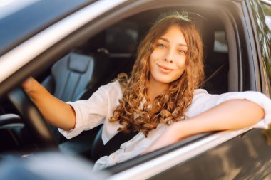 Beyaz bir kaşkorse içinde araba süren güzel kadın pencereden dışarı bakıyor. Genç bir kadın araba kullanıyor ve güneşli havanın tadını çıkarıyor. Ulaşım, seyahat, taksi kavramı.