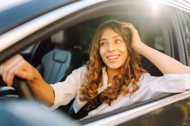 Beyaz bir kaşkorse içinde araba süren güzel kadın pencereden dışarı bakıyor. Genç bir kadın araba kullanıyor ve güneşli havanın tadını çıkarıyor. Ulaşım, seyahat, taksi kavramı.