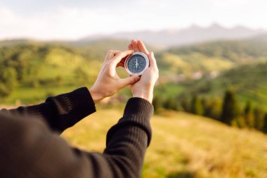 Yeşil tepelere karşı pusula tutan erkek ellerini yaklaştırın. Gezgin pusulayı tutuyor, yönünü arıyor ve dışarıda yeni yerler keşfediyor. Doğa konsepti.