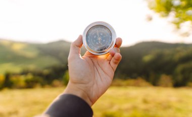 Yeşil tepelere karşı pusula tutan erkek ellerini yaklaştırın. Gezgin pusulayı tutuyor, yönünü arıyor ve dışarıda yeni yerler keşfediyor. Doğa konsepti.