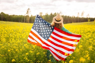 Parlak sarı bir tarlada neşeli bir kadın güneşli bir günde Birleşik Devletler bayrağını tutuyor. Güzel bir kadın özgürlüğü hisseder, kolza tohumu tarlasından zevk alır. Tatil kavramı, eğlence..
