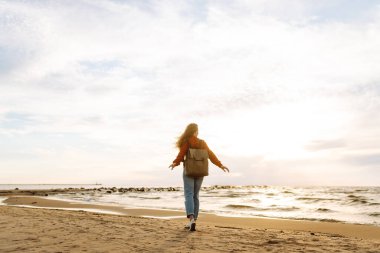 Sırt çantalı gezgin gün batımında sahilde duruyor, özgürlüğü hissediyor. Genç bir kadın kumsalda yürüyor, deniz manzarasının tadını çıkarıyor. Zevk kavramı, özgürlük..