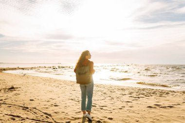 Sırt çantalı gezgin gün batımında sahilde duruyor, özgürlüğü hissediyor. Genç bir kadın kumsalda yürüyor, deniz manzarasının tadını çıkarıyor. Zevk kavramı, özgürlük..