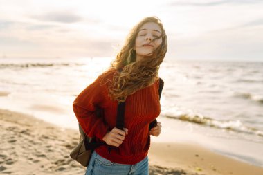 Sırt çantalı gezgin gün batımında sahilde duruyor, özgürlüğü hissediyor. Genç bir kadın kumsalda yürüyor, deniz manzarasının tadını çıkarıyor. Zevk kavramı, özgürlük..