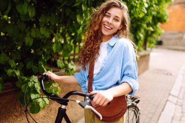 Güneşli şehir caddesinde yürüyüş yapan bisikletli neşeli bir kadın. Avrupa 'da bisikletle gezen bir turist. Aktif yaşam tarzı. Turizm, eğlence konsepti.