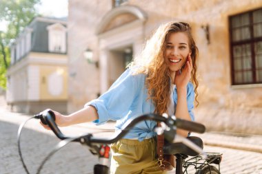 Güneşli şehir caddesinde yürüyüş yapan bisikletli neşeli bir kadın. Avrupa 'da bisikletle gezen bir turist. Aktif yaşam tarzı. Turizm, eğlence konsepti.