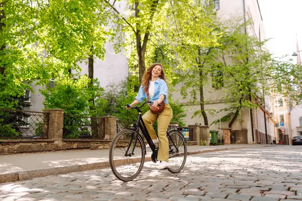 Güneşli şehir caddesinde yürüyüş yapan bisikletli neşeli bir kadın. Avrupa 'da bisikletle gezen bir turist. Aktif yaşam tarzı. Turizm, eğlence konsepti.