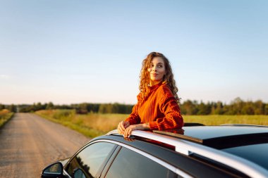 Arabasının camından sarkan neşeli kadın kendini özgür hissediyor. Arabayla seyahat eden genç bir kadın araba penceresinden yolculuğun tadını çıkarıyor. Macera ve ulaşım kavramı.