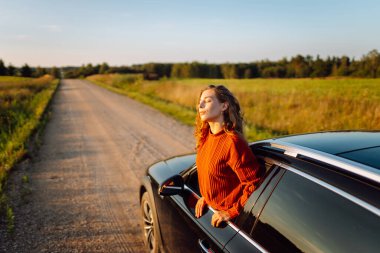 Arabasının camından sarkan neşeli kadın kendini özgür hissediyor. Arabayla seyahat eden genç bir kadın araba penceresinden yolculuğun tadını çıkarıyor. Macera ve ulaşım kavramı.