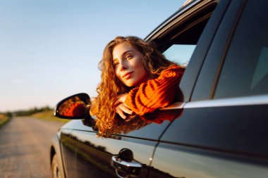 Arabasının camından sarkan neşeli kadın kendini özgür hissediyor. Arabayla seyahat eden genç bir kadın araba penceresinden yolculuğun tadını çıkarıyor. Macera ve ulaşım kavramı.