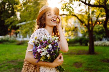Telefonu ve gür bir buket kır çiçeğiyle güzel bir kadın yeşil bir parkta günbatımının tadını çıkarıyor. Şapkalı ve telefonlu bir turist parkta dinlenirken sohbet ediyor ya da blog yazıyor..
