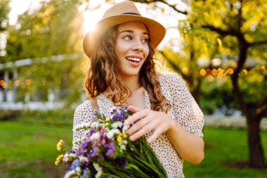 Telefonu ve gür bir buket kır çiçeğiyle güzel bir kadın yeşil bir parkta günbatımının tadını çıkarıyor. Şapkalı ve telefonlu bir turist parkta dinlenirken sohbet ediyor ya da blog yazıyor..