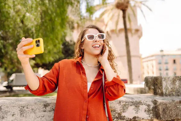 Güneşli şehrin arka sokaklarında selfie çeken şapkalı mutlu kadın portresi. Telefondaki güzel turist blogları, günbatımı yürüyüşünün tadını çıkarıyor. Turizm, blog konsepti.