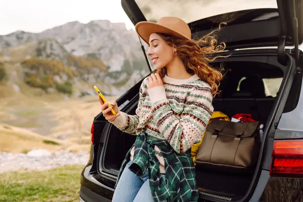 Arabasının bagajında telefonu olan güzel bir kadın yolculukta eğleniyor. Genç bir gezgin, arabadan dağ manzarasını izliyor ve blog yazıyor. Seyahat tutkusu.