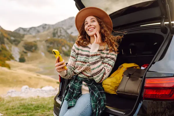 Arabasının bagajında telefonu olan güzel bir kadın yolculukta eğleniyor. Genç bir gezgin, arabadan dağ manzarasını izliyor ve blog yazıyor. Seyahat tutkusu.