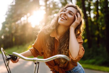 Ormanda, güneşin altında bisiklet süren mutlu bir kadın var. Güzel bir kadın gün batımında bisiklet sürmekten zevk alıyor, dinleniyor. Aktif yaşam tarzı. Hafta sonu konsepti.