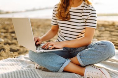 Gün batımında elinde dizüstü bilgisayarla sahilde oturan bir kadının portresi. Dizüstü bilgisayarda çalışan, klavyede dışarıda oturan güzel bir bayan serbest yazar. Bağımsız kavram, doğa ve rahatlama.